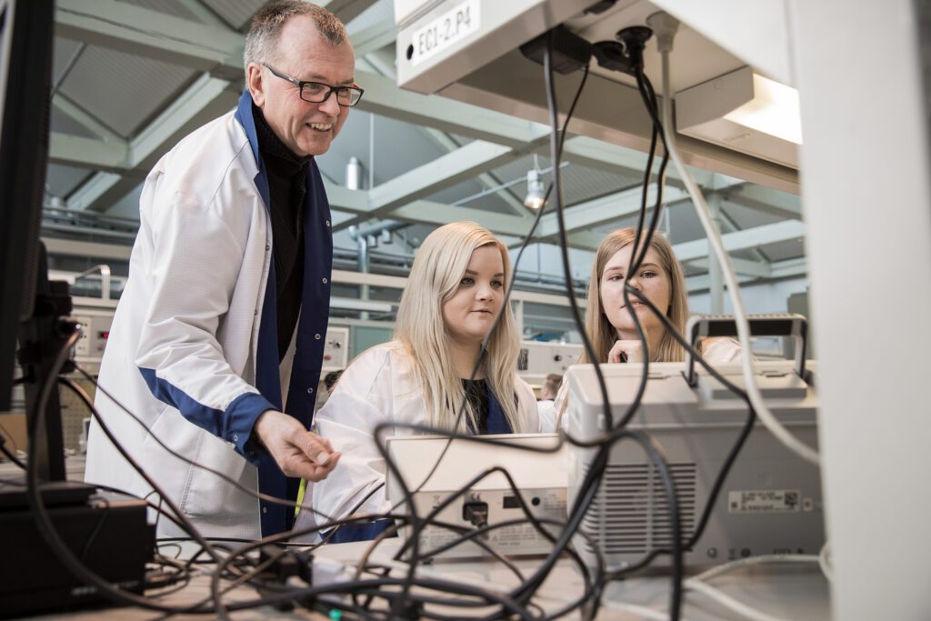 sähkötekniikan opiskelijoita tekniikan laboratoriossa, jossa opettaja ohjaa opiskleijoita.